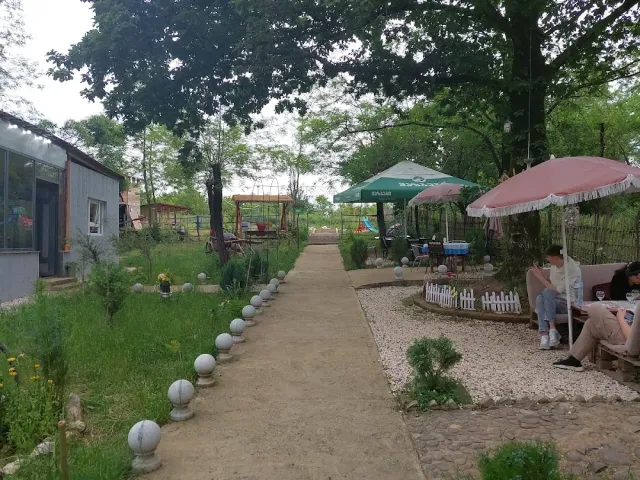 A garden path with globe lamps, pink and green parasols, people sitting and a play structure