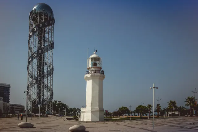 A tall tower wrapped in a spiral of letters beside a white lighthouse on the promenade