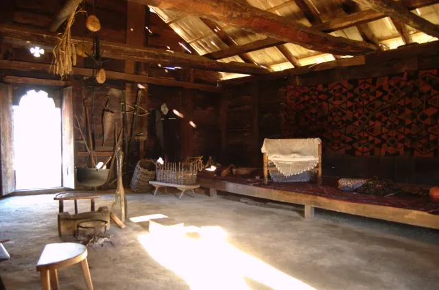 The interior of a traditional wooden house with roof beams, a cradle, benches and old household tools