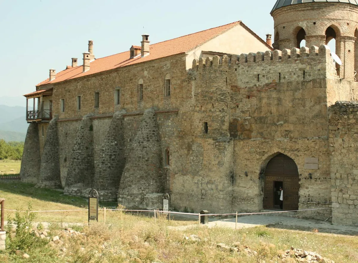 A fortified monastery wall with an arched gate and a red tiled roof in bright daylight