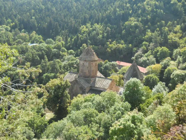 A domed stone monastery with low buildings on a steep wooded slope