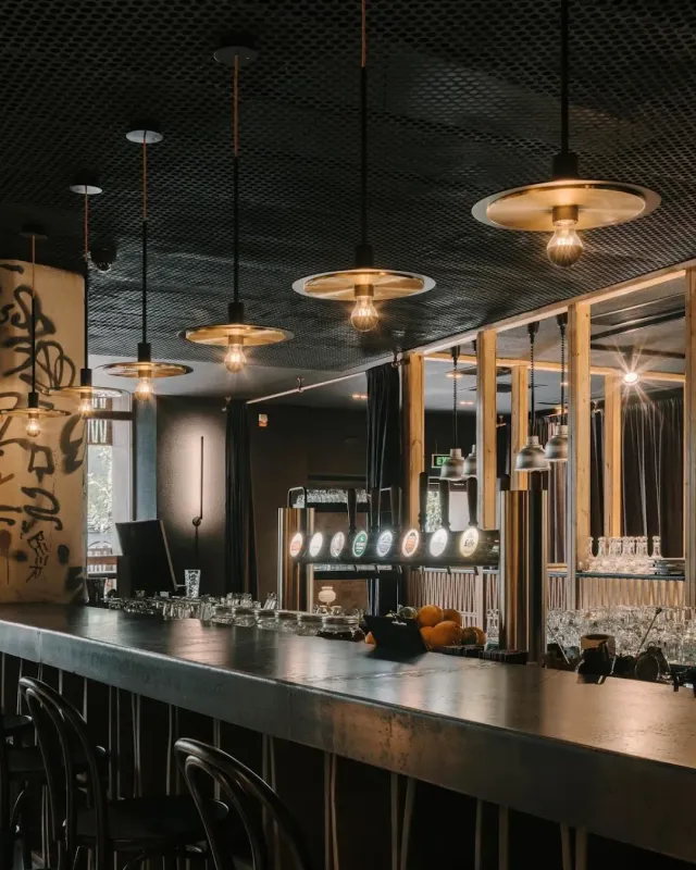 A long dark bar counter with hanging lamps, beer taps and rows of glasses