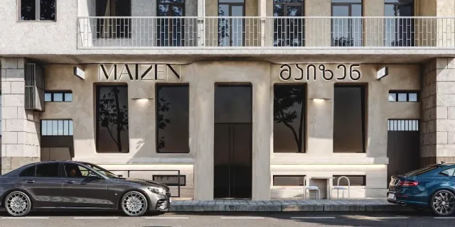 A minimal pale stone facade with metal lettering on the wall and cars parked in front of it