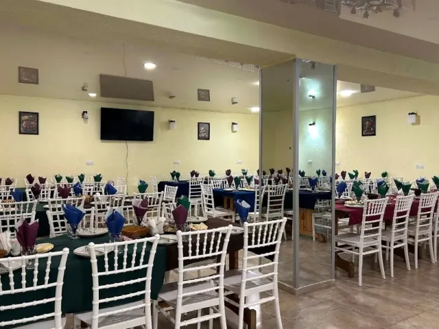 A hall with rows of tables in green and burgundy cloths, white chairs and folded napkins