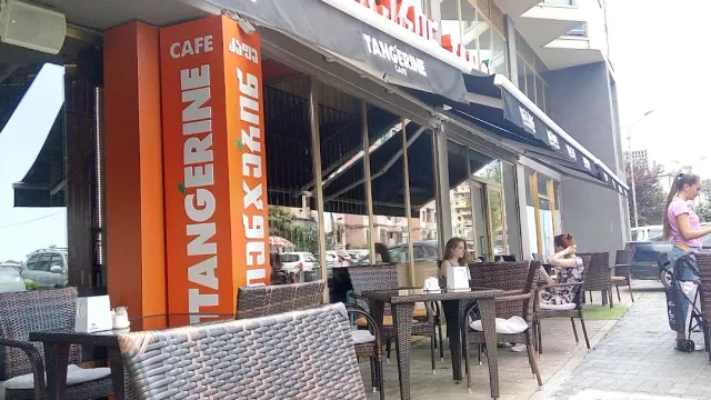 A street terrace with wicker chairs, a tall orange sign and diners at the tables