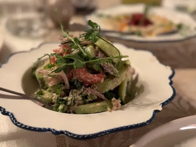 A cucumber and tomato salad in a walnut dressing with green leaves, in a white bowl with blue edges