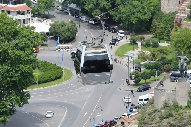 A glass cable car cabin gliding above a green city junction