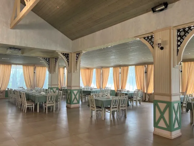 A large hall with a wooden ceiling, white columns, peach curtains and long set tables