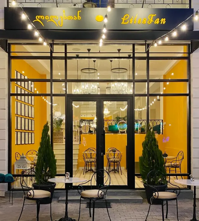 A glass front lit at night with yellow walls, chandeliers, strings of bulbs and metal chairs