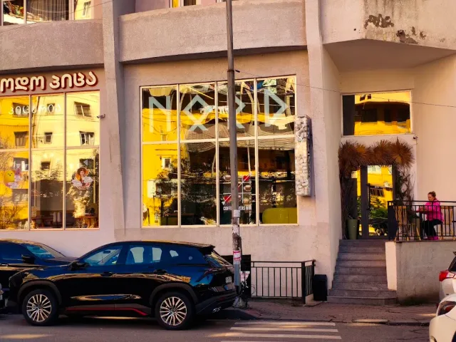 A building facade with large windows glowing at sunset, parked cars and steps at the side