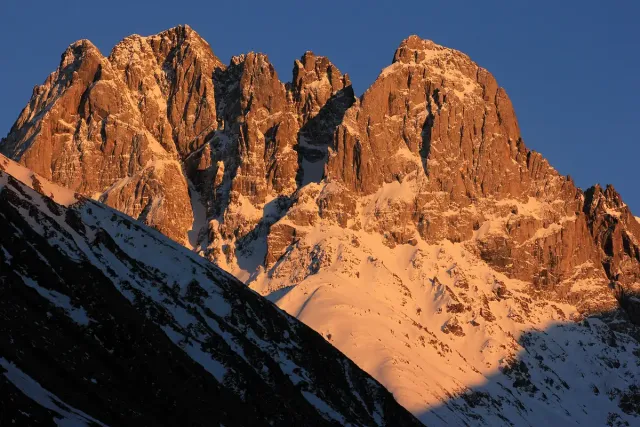 Jagged rock spires glowing orange at sunset above a snow covered slope