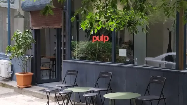 A dark facade with red lettering on the window, folding chairs and round tables on the sidewalk