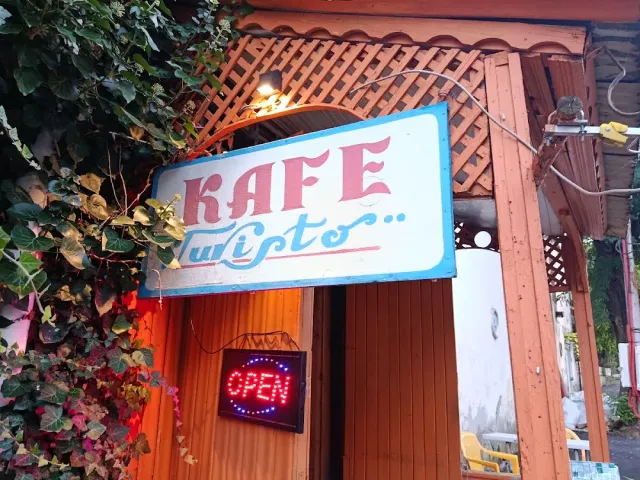 A hand painted sign above a wooden entrance with a latticed arch, a lit sign and flowering ivy