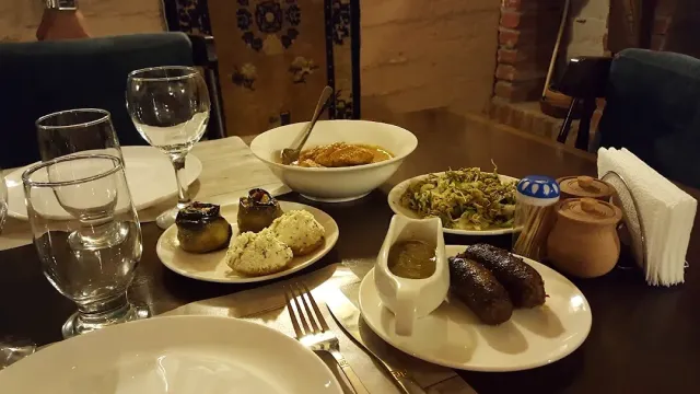 A table with a bowl of stew, stuffed vegetables, salad, sausages in sauce and a clay jug