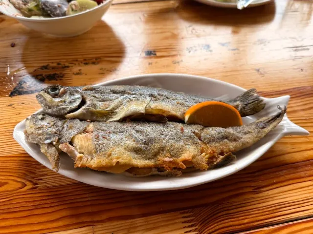 Two fried fish on an oval plate with a lemon wedge, on a wooden table