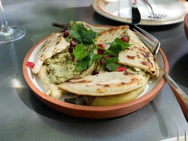 A folded cheese pastry with a green spread, parsley and pomegranate seeds in a clay bowl