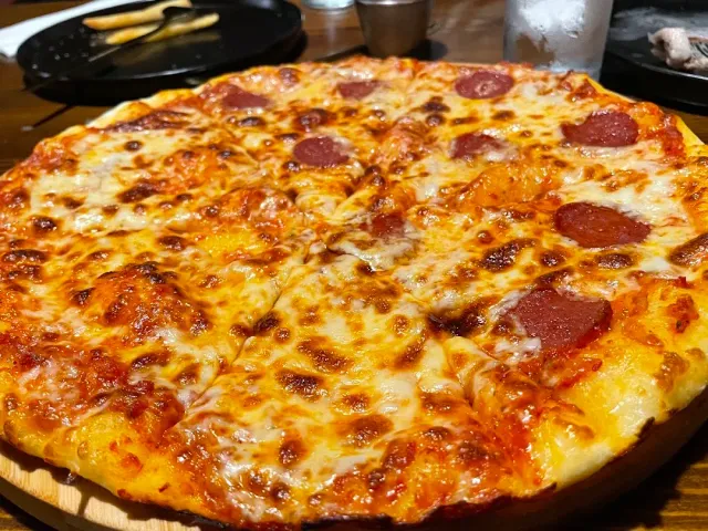 A large pizza with melted cheese and red sausage slices on a wooden board