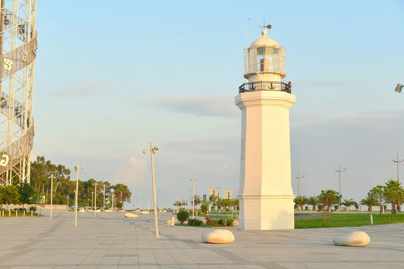 The pale octagonal tower of the Batumi lighthouse standing on the paved promenade at the end of the seaside boulevard