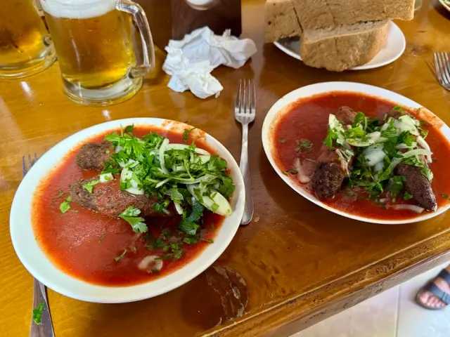 Two plates of meat patties in tomato sauce with herbs and onion, a glass of beer and bread