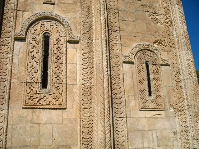 Two narrow windows in a stone wall framed by rich geometric carving