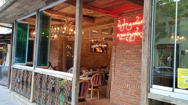 A front open to the street with red lit lettering, an antler chandelier and a brick wall