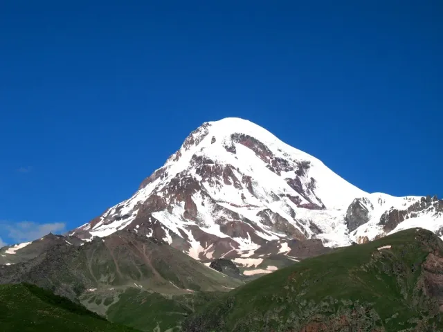 A sharp snow covered peak above a rocky ridge under a blue sky