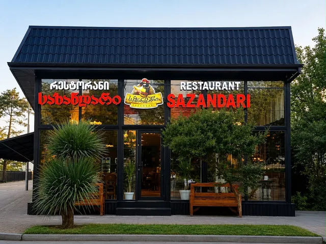 A dark glass facade with a prominent red sign, a wooden bench and trees at the entrance