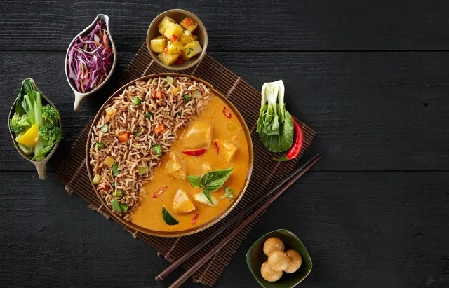 A dish of rice and orange sauce in a bowl on a bamboo mat, beside sides in small bowls