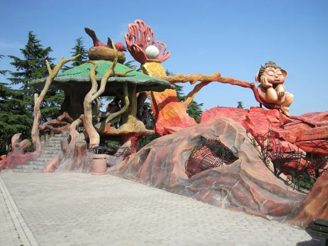 A sculpted amusement park attraction of mushrooms and branches with a sleeping figure on a red rock