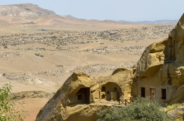 Cave cells carved into a sandstone cliff in a rolling desert landscape