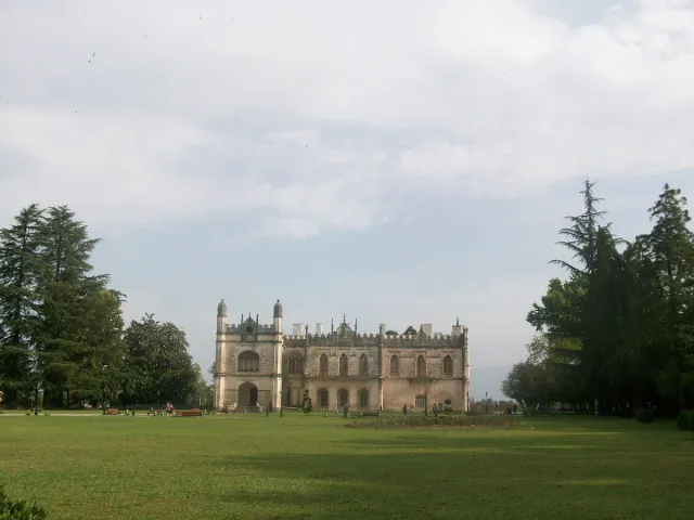 A two storey stone palace at the far end of a wide lawn ringed by trees