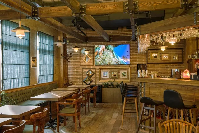 A space with wooden beams, a brick wall, wooden tables and a bar counter with high stools