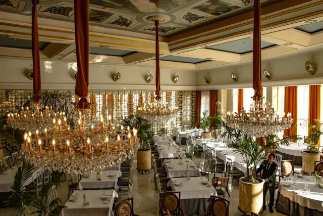 A grand hall with a painted ceiling, huge crystal chandeliers and tables in white cloths