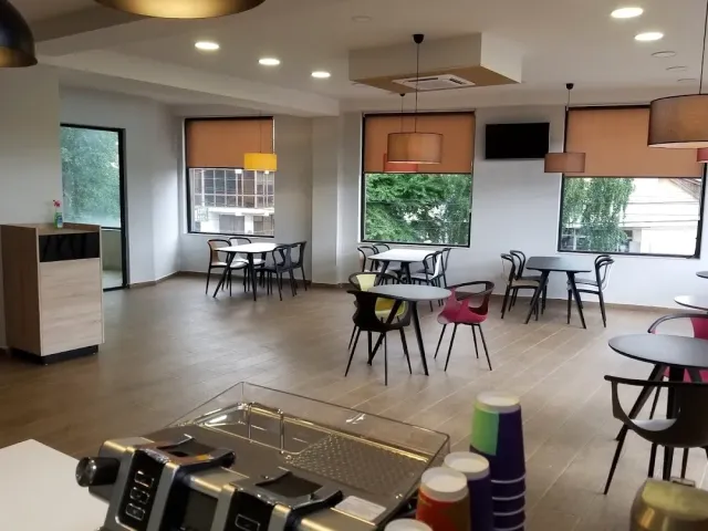 A bright hall with empty tables and chairs, orange blinds and a counter with colorful cups