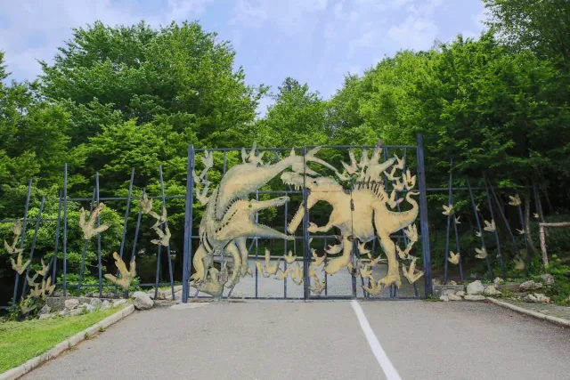 An iron gate with dinosaur figures at the entrance, dense forest behind it