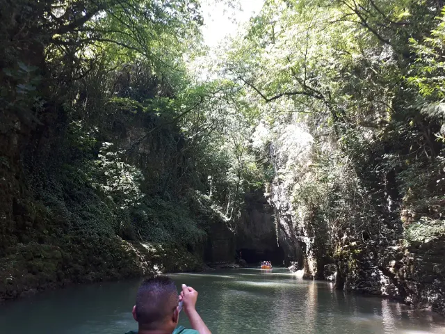Turquoise water in a narrow canyon with vegetation hanging from the cliffs and a boat in the distance