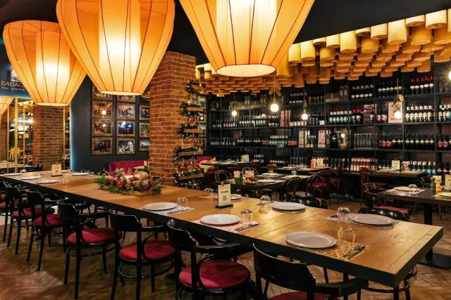 Huge fabric lampshades above a long table with red chairs, and walls packed with bottles