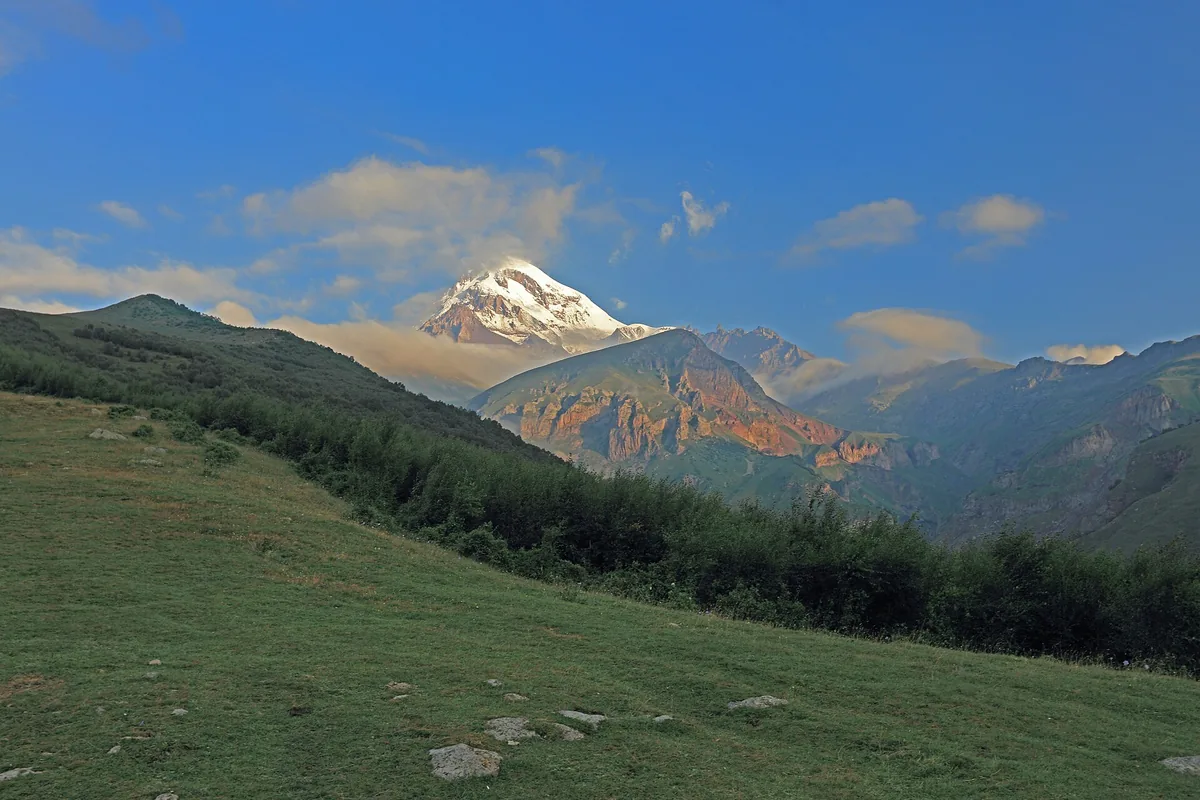 A snow capped peak in morning light above pasture