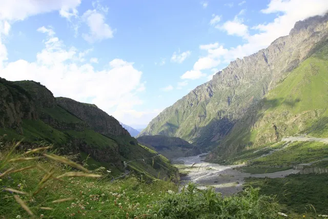 A wide green gorge between steep ridges with a river running along its floor