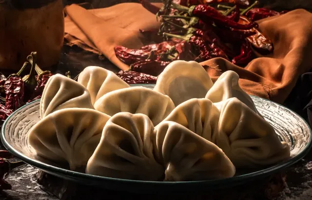 Folded dough dumplings on a plate, with dried red peppers and brown cloth behind