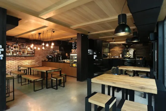 An interior with wooden tables, a brick wall and a roasting machine behind the counter