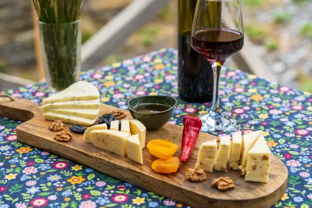 A wooden board with slices of cheese, walnuts, dried apricots and honey, beside a wine bottle