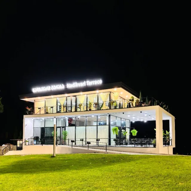 A two story glass building lit at night with a sign on the roof and a lawn in front