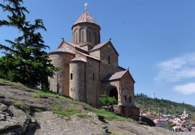 A stone church with a pointed dome on the edge of a cliff above the city