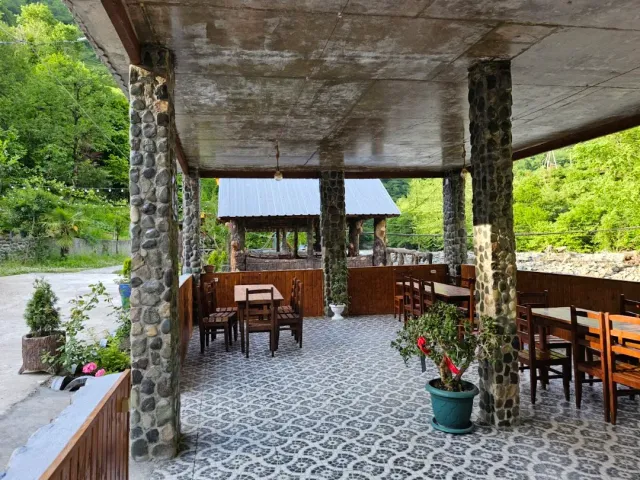 A covered terrace with stone pillars, wooden tables, a tiled floor and a view of green hills