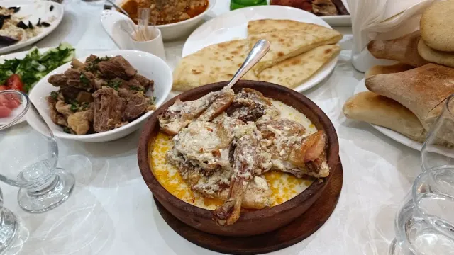 A clay pot with chicken in a white sauce, beside a meat stew, flatbreads and salad
