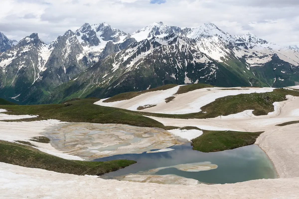 Shallow mountain lakes among patches of snow, facing a ridge of snowcapped peaks