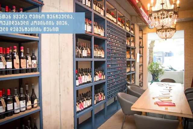 A wine shop with blue shelves full of bottles, a rack wall and a long tasting table