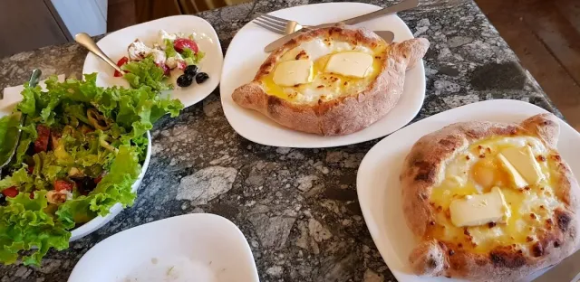Two dough boats filled with cheese topped with yolk and butter, beside a bowl of green salad
