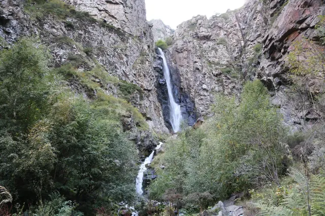 A slender waterfall dropping down a high cliff inside a wooded gorge